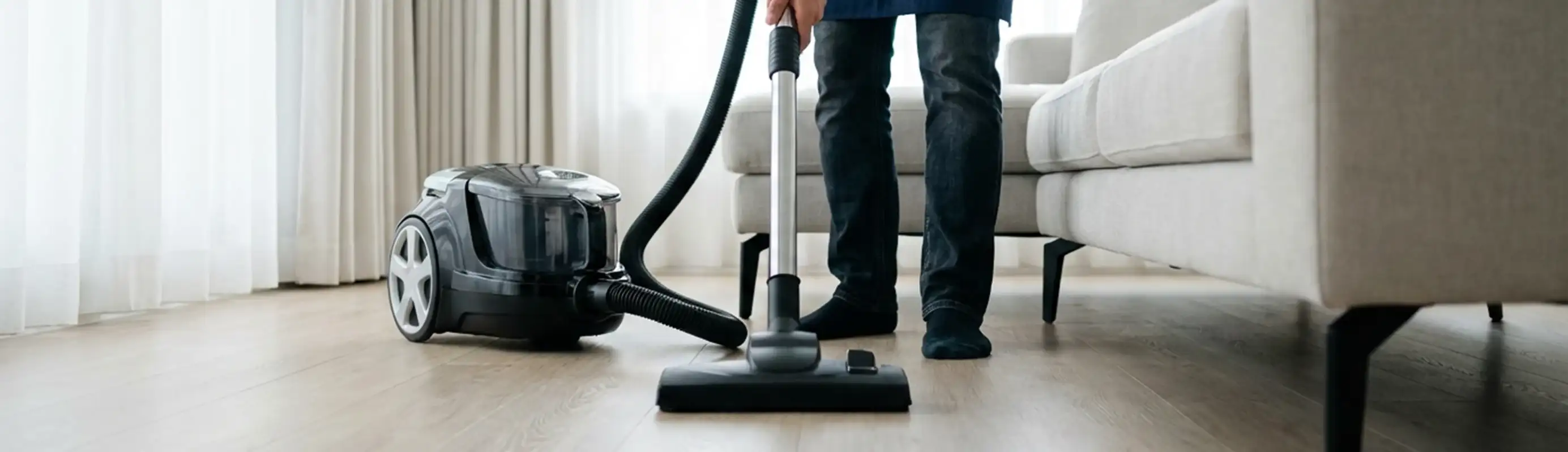 Professional house cleaner vacuuming a living room floor with a canister vacuum cleaner, Little Rock, AR.