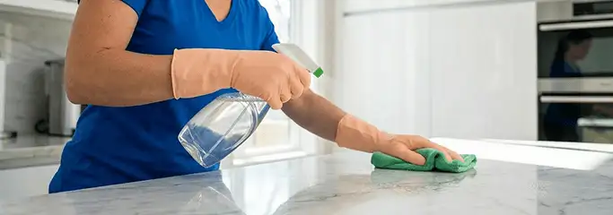 Maid service worker spraying and wiping a kitchen countertop with a microfiber cloth for sanitizing, Little Rock, AR.