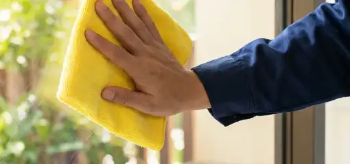 House cleaner wiping a glass window with a yellow microfiber cloth for streak-free cleaning, Little Rock, AR.